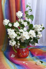 A bouquet of snow-white jasmine in a vase with a heart on the background of a beautiful bright and white transparent drapery. Beauty!