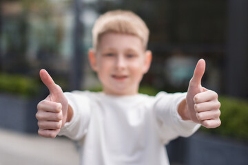 focus on hands of school boy in white sweatshirt show two thumb up gesture on city background