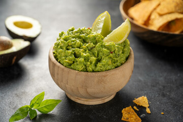 Guacamole avocado mash dip, with tortilla chips. Dark background.