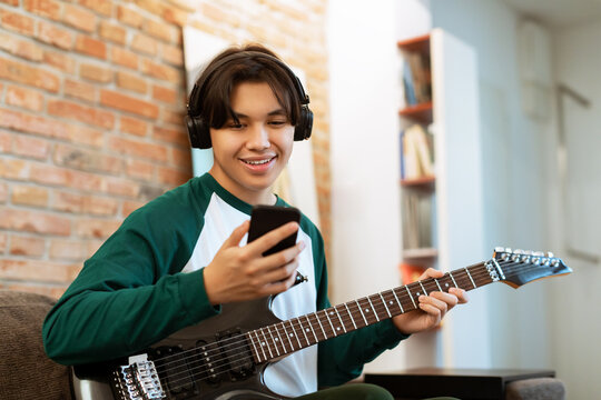 Japanese Guy Plays Electric Guitar Watching Tutorial on Cellphone Indoor