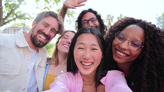Group of joyful young friends waving hands and do greetings looking at camera enjoying the weekend on a social gathering. Multiracial happy people taking a selfie portrait smiling together at party
