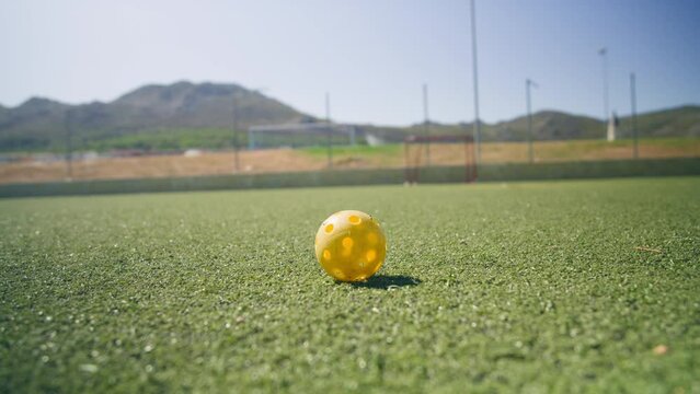A yellow floorball lying outdoors ona green sports field