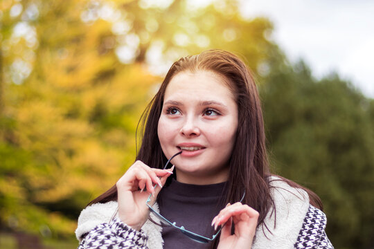 A young woman with a smile on her face, taking off her sunglasses, remembers pleasant moments.