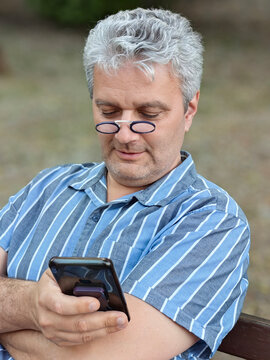 Portrait of an senior man sitting on a bench in a public park and using his smartphone.