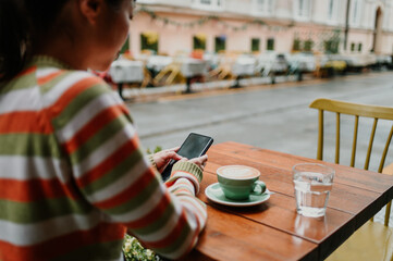 Girl enjoying her free time while sitting in a cafe bar and holding her phone.
