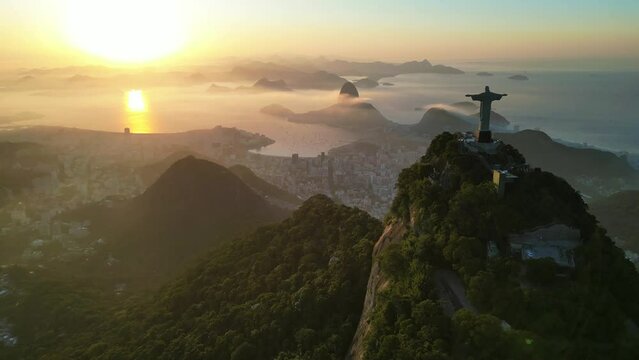 Rio de Janeiro, Brazil - June 10, 2023: Aerial view of Christ the Redeemer statue on top of the Corcovado Mountain with the Sugarloaf Mountain in the horizon on sunrise.
