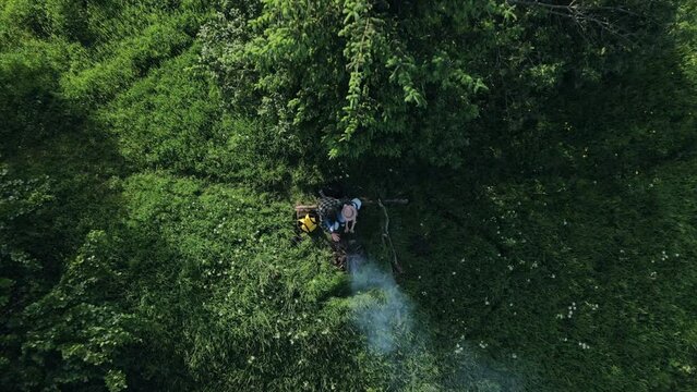 Aerial drone view of young father and little daughter in hat warming up hands next to campfire in forest at summertime. Hiking, adventure active vacations, camping vibes and outdoor lifestyle mood