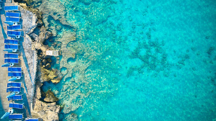 Top down aerial view of deck chairs on a beach in the morning. Aerial view of blue crystal clear lagoon