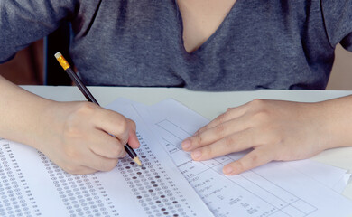 Students hand holding pencil writing selected choice on answer sheets and Mathematics question sheets. students testing doing examination. school exam