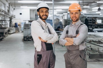Two international male workers in overalls on the background of the production of PVC windows and...
