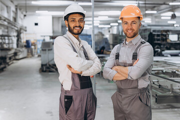 Two international male workers in overalls on the background of the production of PVC windows and doors