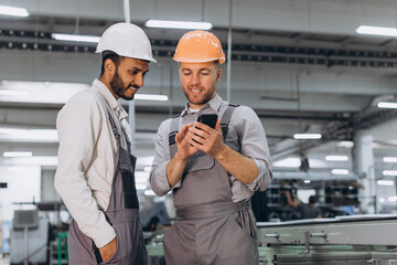 Two international male workers in overalls looking at the phone against the background of the...