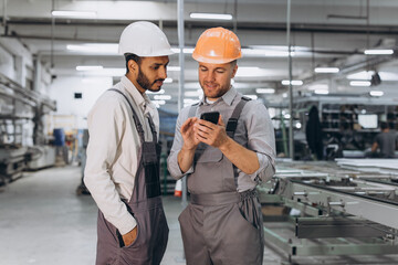 Two international male workers in overalls looking at the phone against the background of the...