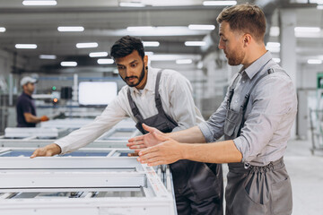 Two male international workers in overalls work together at a machine for the production of...