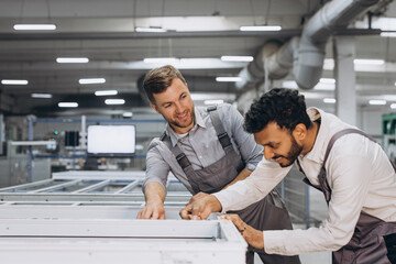 Two male international workers in overalls work together at a machine for the production of...