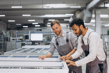 Two male international workers in overalls work together at a machine for the production of...