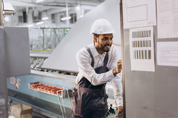 Operator of machine. Industrial worker indoors in factory. Young technician in white hard hat.