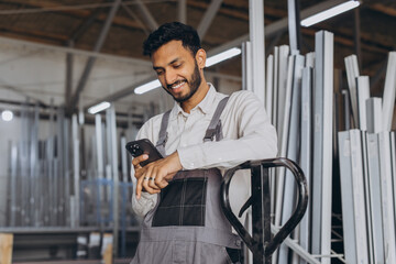 Portrait of a happy Hindu worker in a white helmet and overalls holding a hydraulic truck and...