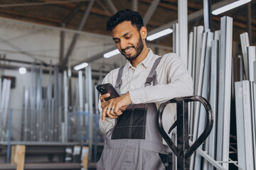 Portrait of a happy Hindu worker in a white helmet and overalls holding a hydraulic truck and...