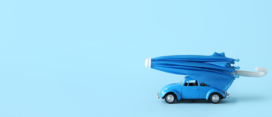 Toy car and mini umbrella on light blue background with space for text