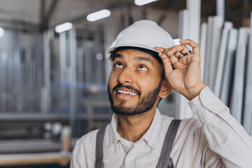 Portrait of a happy Hindu worker in a white hard hat and overalls holding a hydraulic truck against...