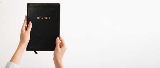 Female hands holding Holy Bible on light background with space for text