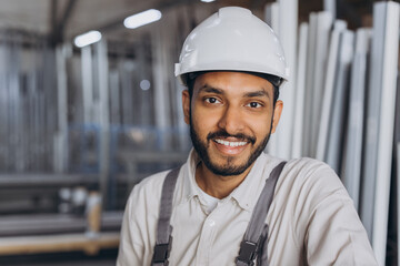 Portrait of a happy Hindu worker in a white hard hat and overalls holding a hydraulic truck against...