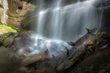 Long exposure waterfall scene with fallen tree log and rainbow