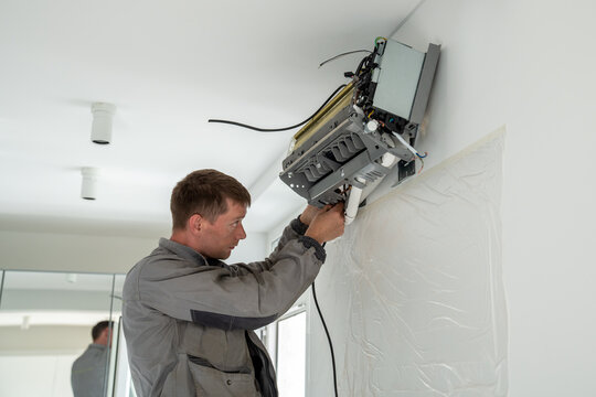 Man technician worker in uniform fixing repairing apartment air conditioner, installing wall-mounted mini split. AC unit maintenance concept