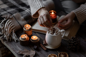 Autumn cozy home composition with hot chocolate with marshmallow and candles. Aromatherapy on a grey fall morning, atmosphere of cosiness and relax. Wooden background, books, close up.