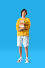 Fototapeta na wymiar Teenage boy with stack of books on blue background