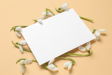 Beautiful snowdrops and blank greeting card on beige background