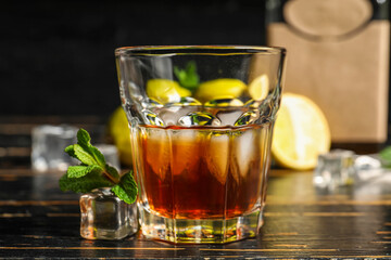 Glass of rum with ice cubes on dark wooden background, closeup