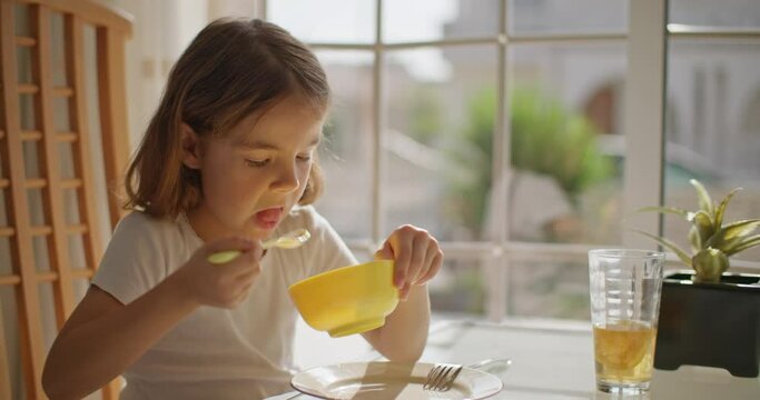 Baby girl eats breakfast and drinks orange juice in the kitchen at breakfast. Delicious nutritious and healthy morning food. High quality 4k footage