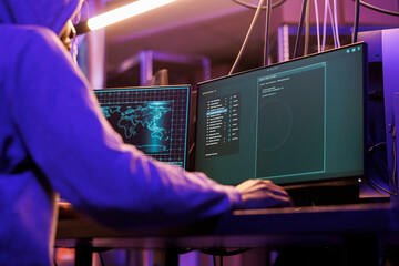 Internet thief using spyware to steal information from victim computer. Young hacker running malicious software code on screen to break into server in abandoned warehouse