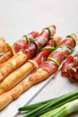 Board of tasty Italian Grissini with bacon on light background, closeup