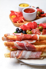 Plate of tasty Italian Grissini with bacon on light background, closeup