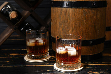 Glasses of cold rum and barrel on dark wooden background