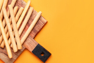 Wooden board with tasty Italian Grissini on orange background, closeup