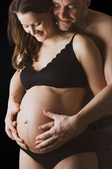 Smiling parents holding naked round belly of pregnant mother in underwear. Last month of pregnancy...