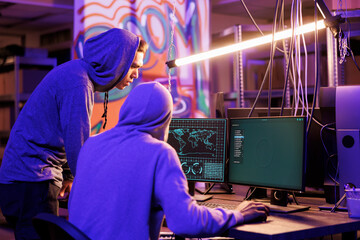 Two hackers in hoods breaking into network system and accessing dark web. Young cybercriminals cracking server password and searching for confidential information to steal