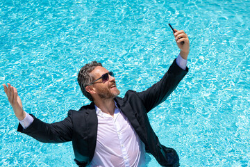 Hot business. Funny excited office worker with phone. Business man in suit used phone in beach. Travel and business. Crazy excited office worker taking a selfie at the beach. Businessman on summer.