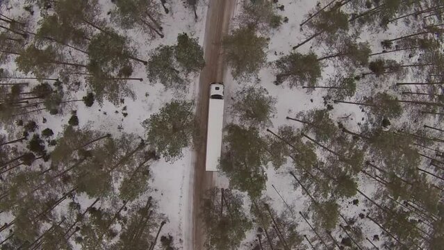drone wide shot of a big white truck driving on a forest road in winter