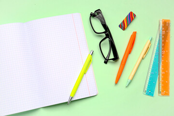 Blank copybook pages, glasses and stationery on green background