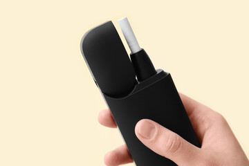 Female hand holding modern electronic cigar with stick on beige background