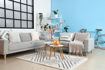 Interior of stylish living room with grey sofas and blooming sakura branches on coffee table
