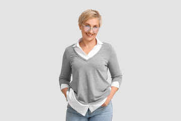 Mature blonde woman in eyeglasses on light background