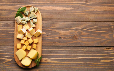 Board with pieces of tasty cheese on wooden background