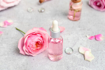 Bottles of cosmetic oil with rose extract and flowers on white table