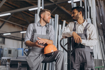Portrait of two international workers wearing hardhats taking break from work and resting speaking to each other on a factory background with copy space
